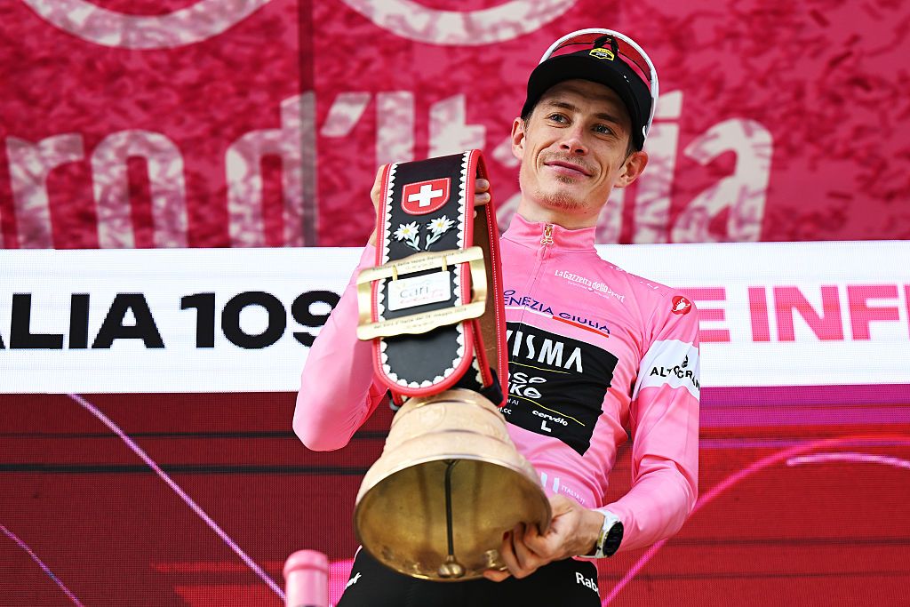 Jonas Vingegaard in the pink jersey on the podium holds a huge bell as prize by the Swiss hosts
