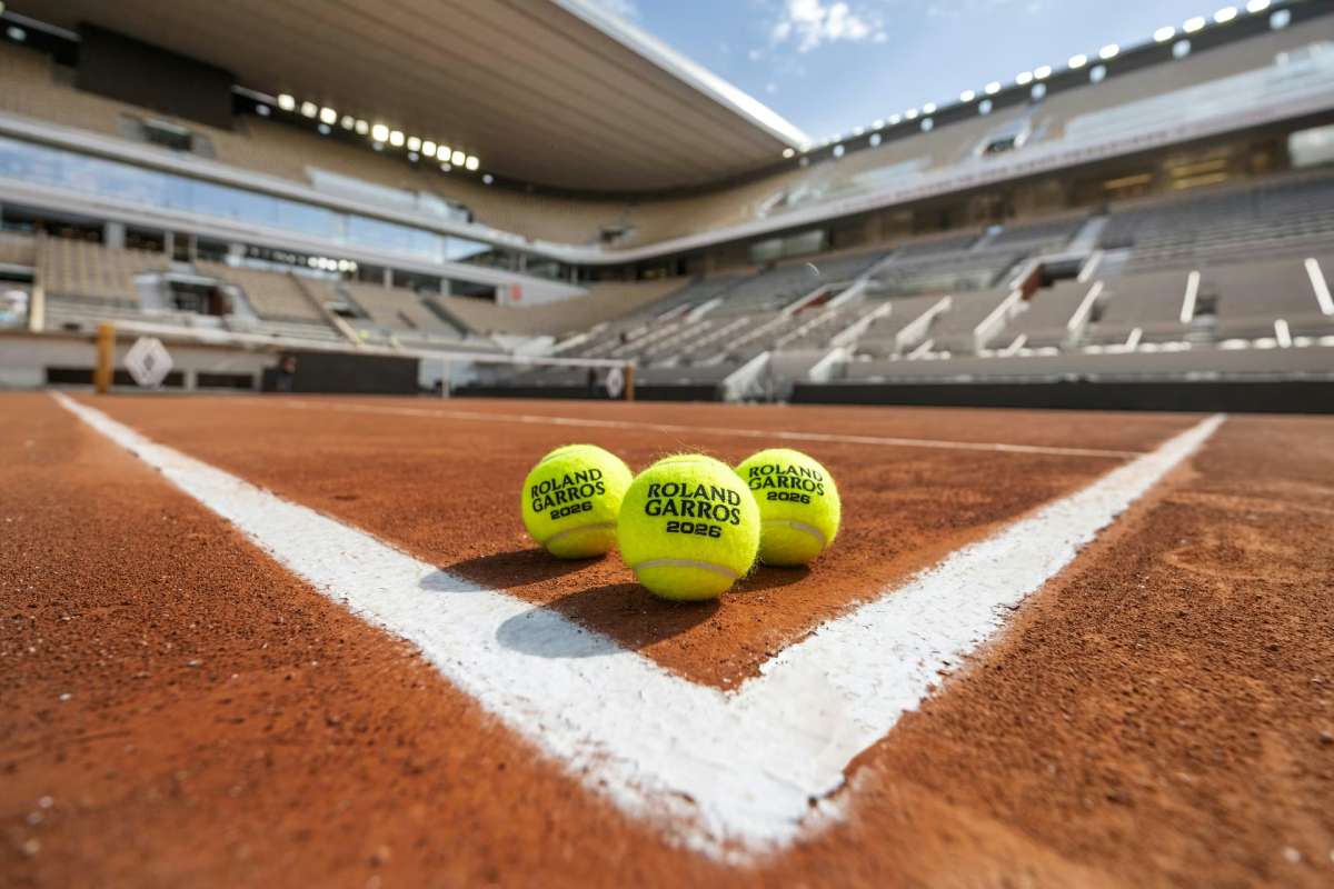Three bright yellow tennis balls with Roland Garros branding on a red clay court near the white line inside an empty stadium.