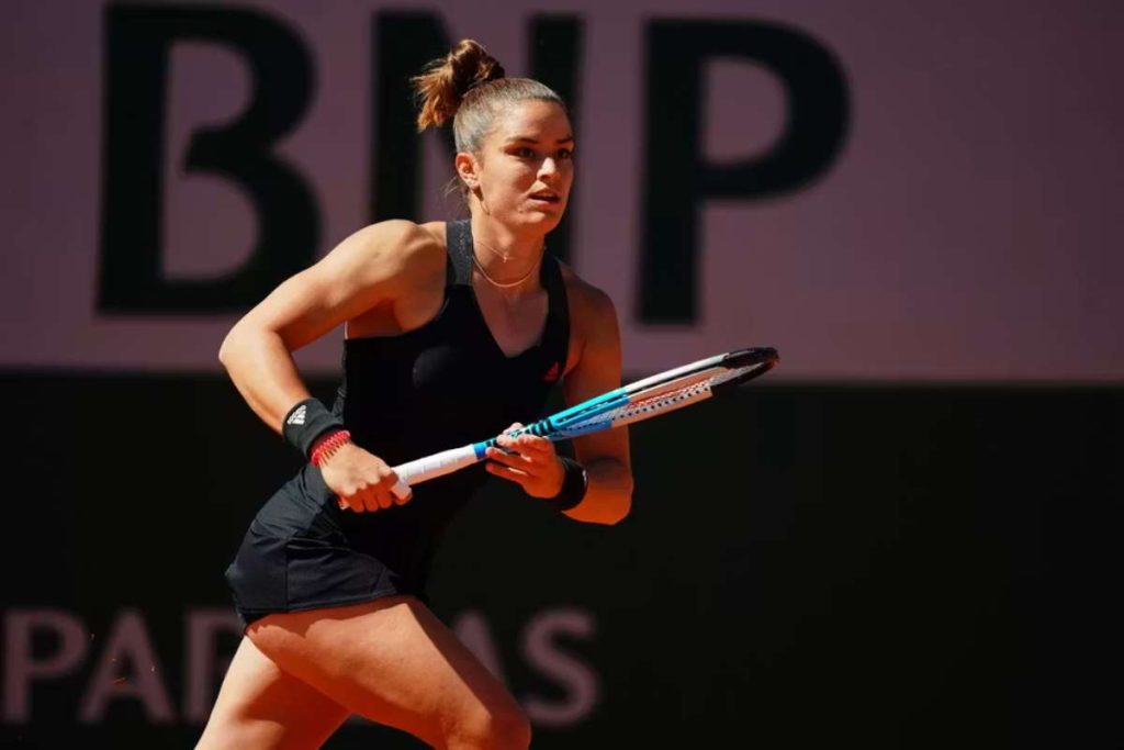 Female tennis player in a black outfit mid-swing on a court, gripping a racket with focused expression.