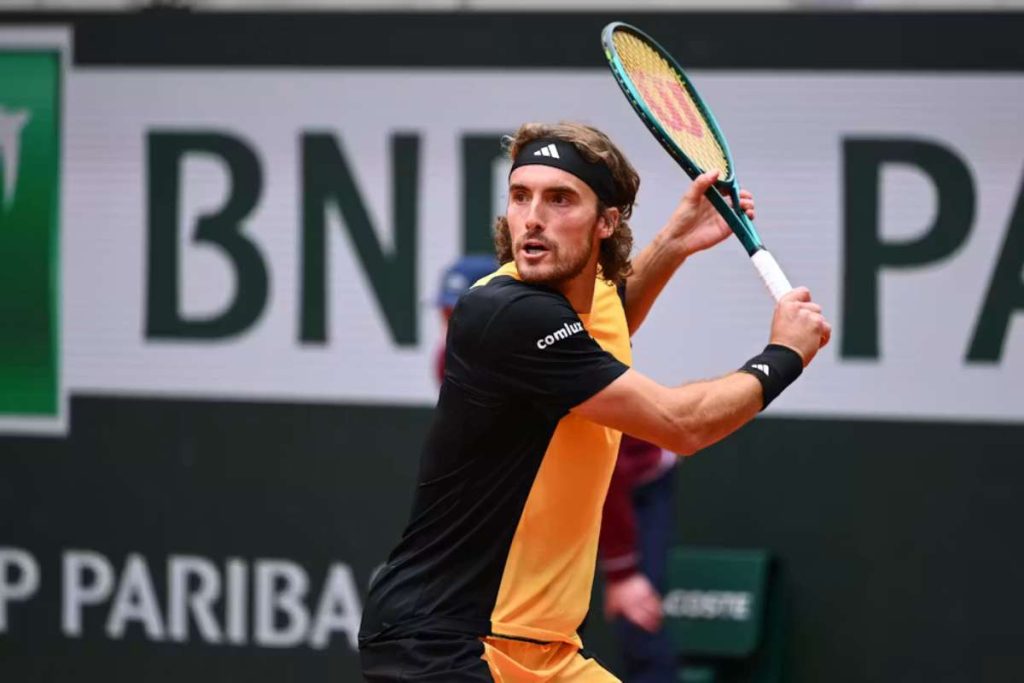 Male tennis player in black and orange outfit prepares to hit a backhand on a court with BNP Paribas signage behind him.