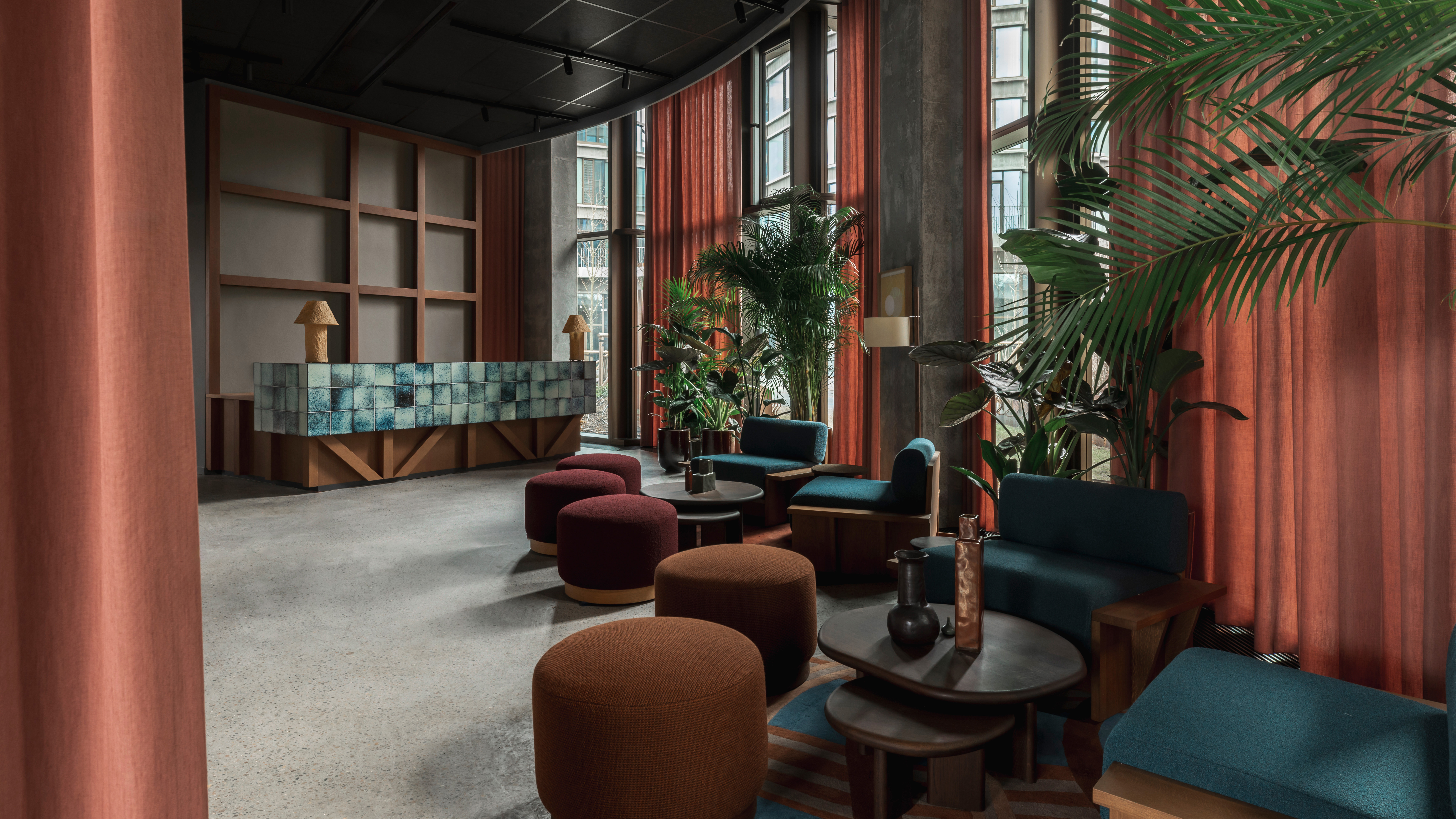A brutalist shell of a hotel where cement walls and tall ceilings are softened by warm woods, textural fabrics, soft forms, and pendant lighting in earthy tones.