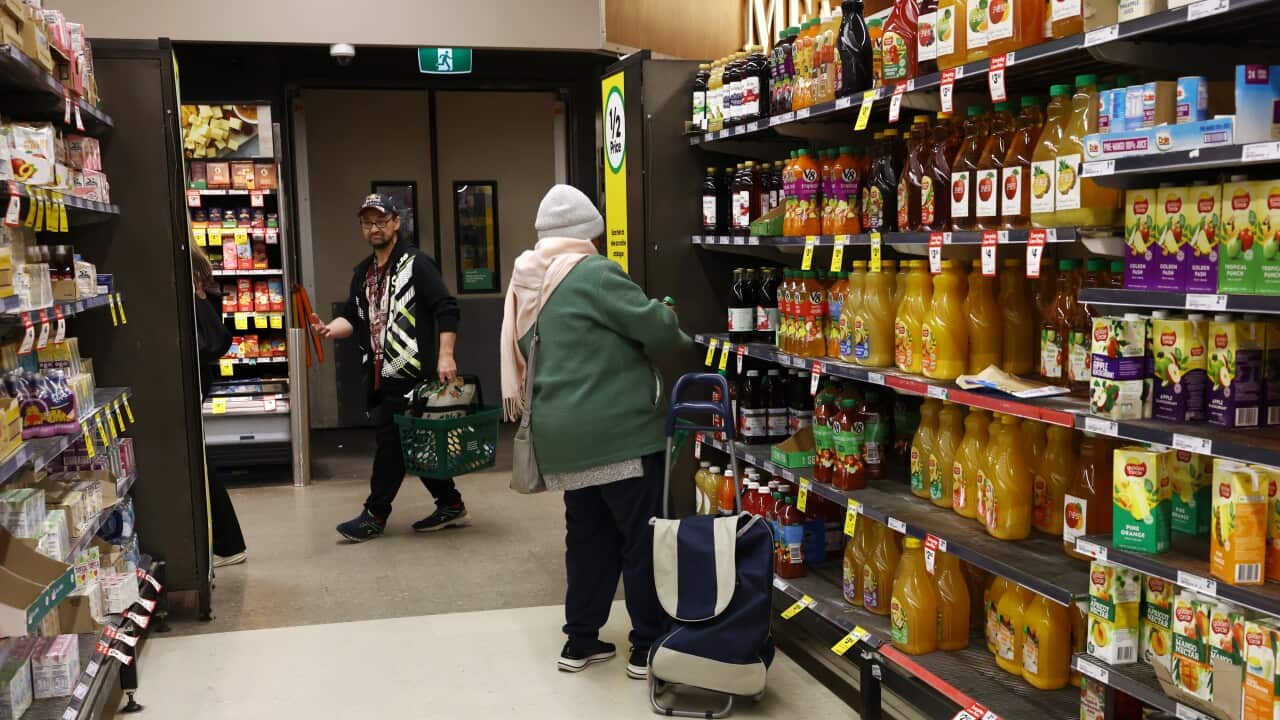 A person browses products at a supermarket aisle with another person seen with a shopping basket in the background