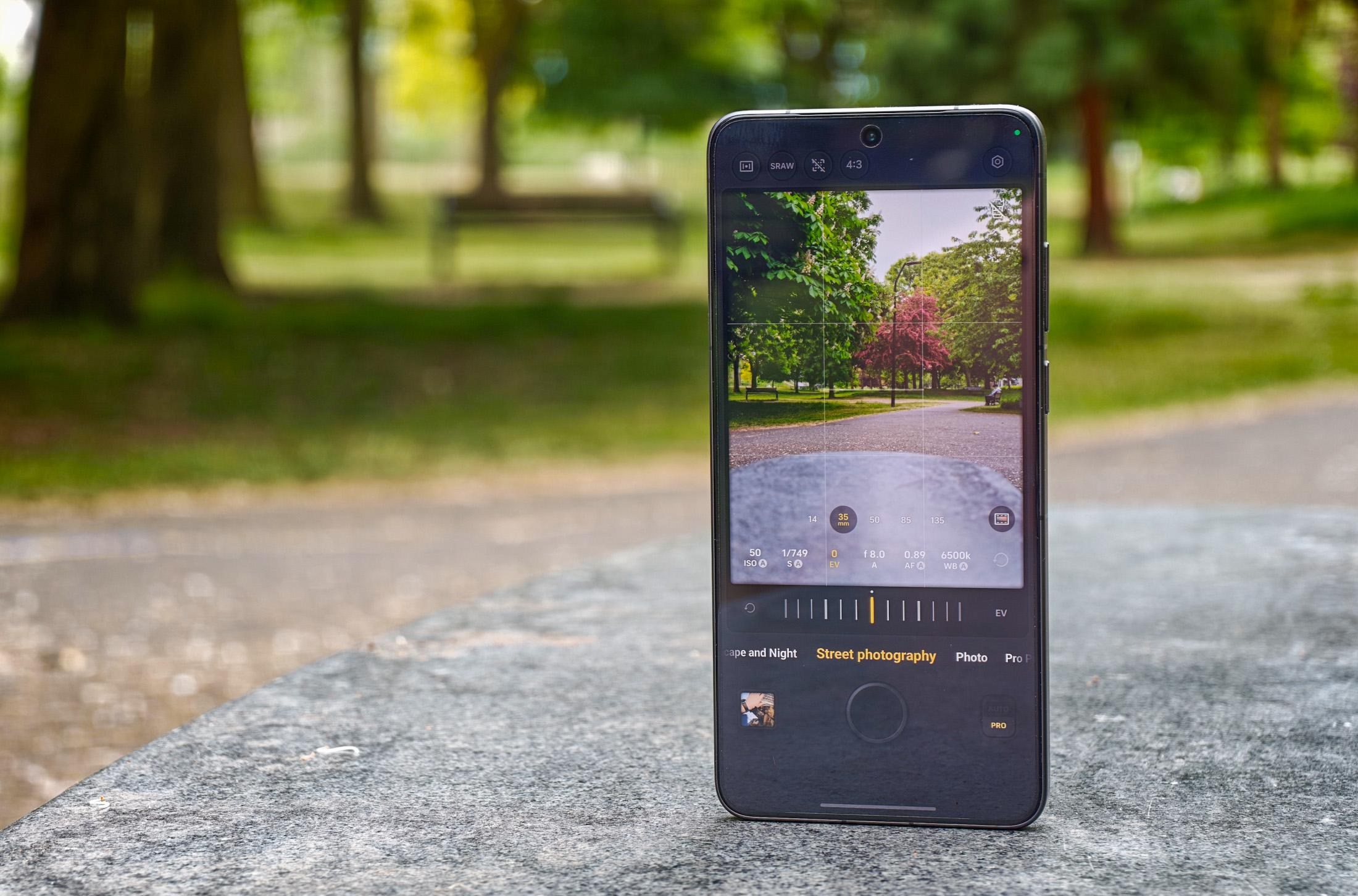 Photo of the Vivo X300 Ultra standing on a gray stone bench showing the Street photography mode, with the camera pointing at a red tree.