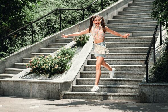 Young woman jumping on outdoor stairs in casual summer outfit smiling and enjoying a sunny park day in the city with carefree energy Young woman jumping on outdoor stairs in casual summer outfit smiling and enjoying a sunny park day in the city with carefree energy