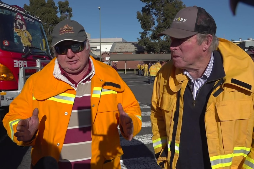 two men in fire fighting outfits face camera