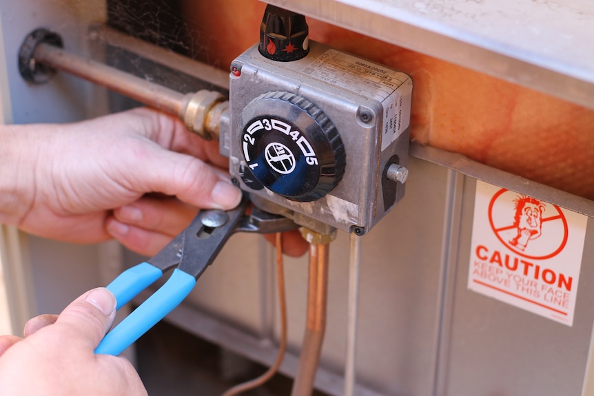 close-up plumber's hands using pliers to adjust gas hot water system