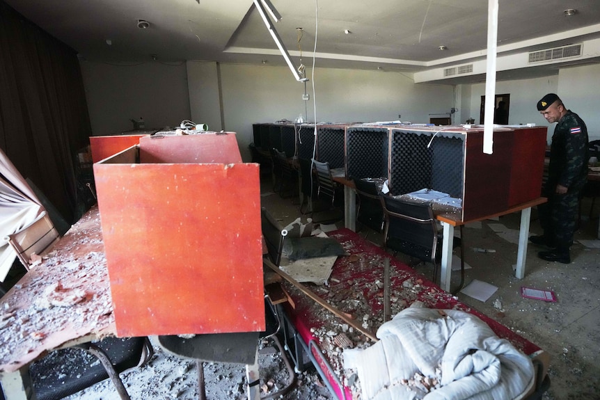 A soldier with a dark beret and Thai flag on his sleeve looks at one of many desks covered with foam soundproofing.