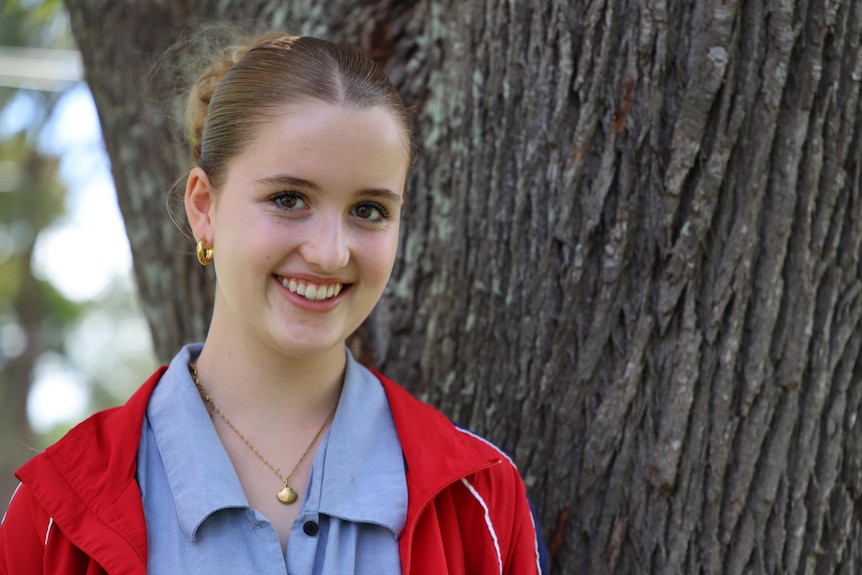 A schoolgirl smiling in front of a tree