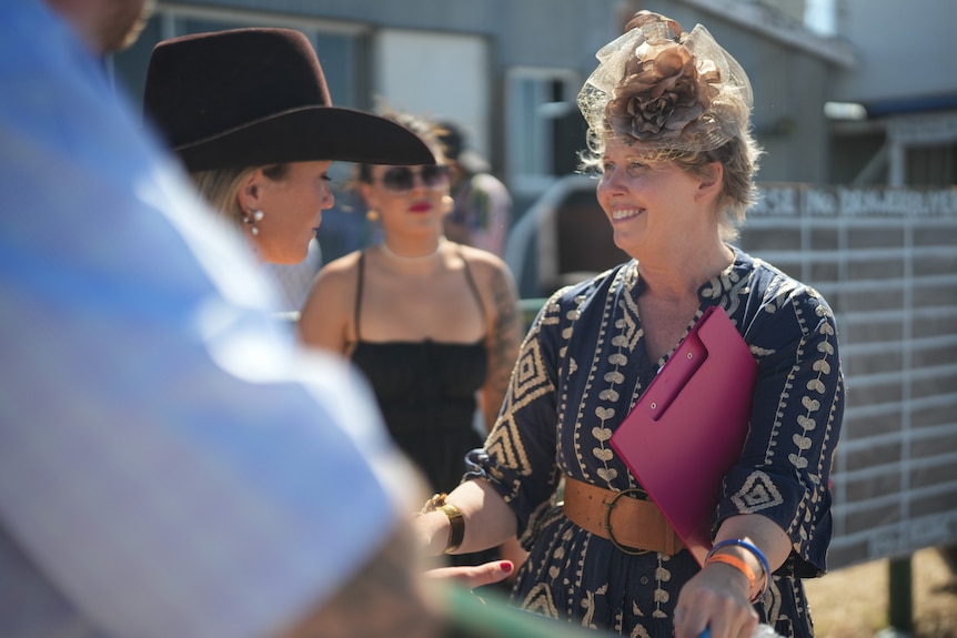 Woman dressed up for outback races smiles while talking to another woman