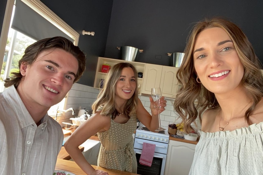 A selfie photo taken in a kitchen showing a young man and two young women. All are smiling.