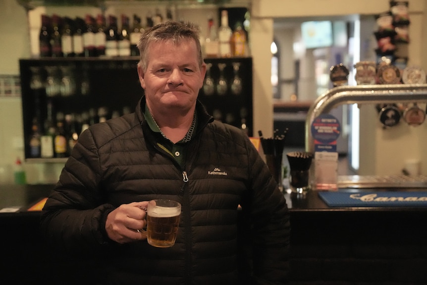A man holds a beer at a bar.