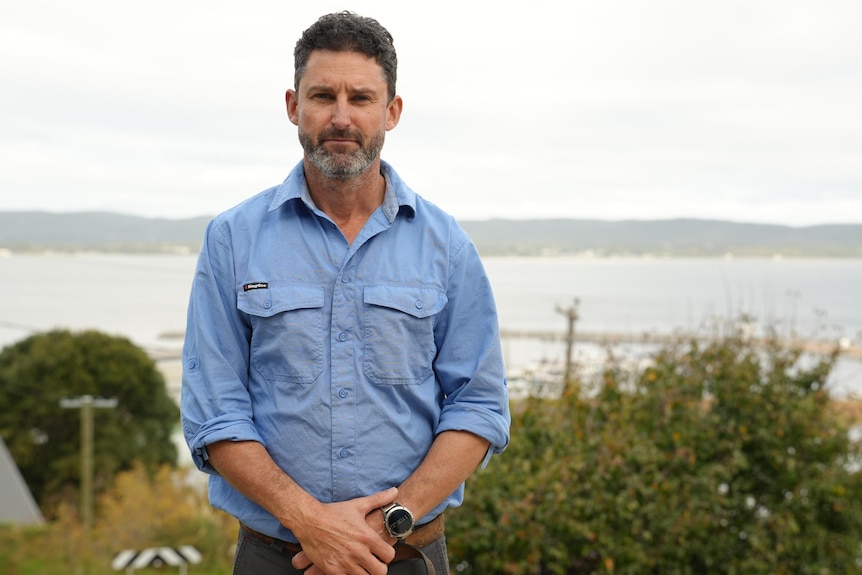 A man with hands crossed in front of him and ocean in background looking at camera