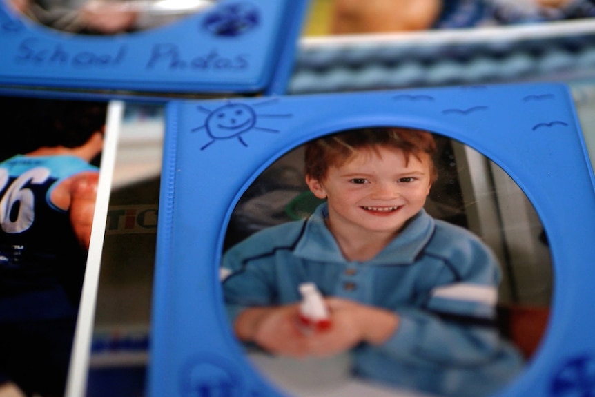 A photo in a frame of a smiling young boy. Underneath it are other photos.