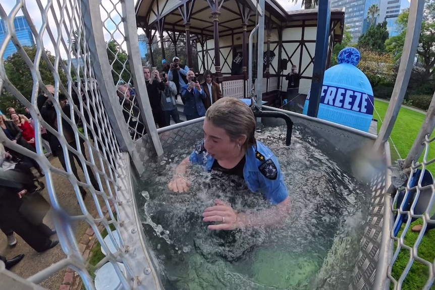 A drenched woman stands chest height in water inside a steel cage as people watch on.