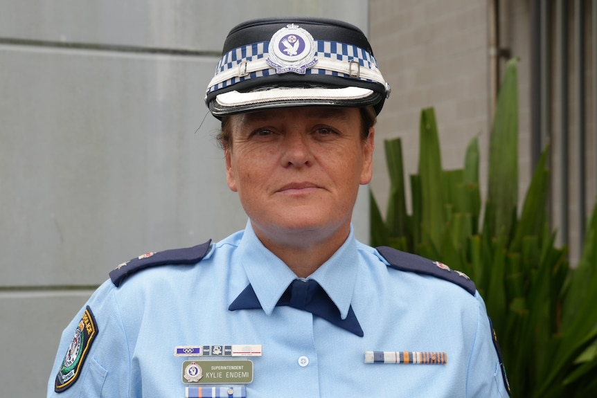 A policewoman in uniform and a police hat looking at the camera.