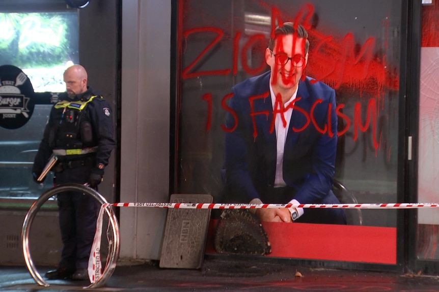 A police officer stands near a wall painted with the words "Zionism is Fascism".