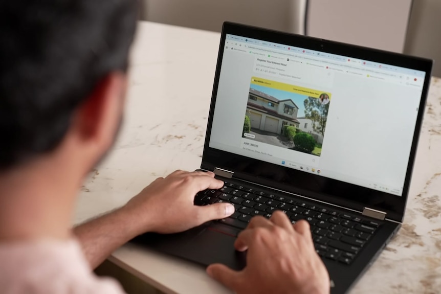 A man pictured from the back looking at a webpage on his laptop as he types.