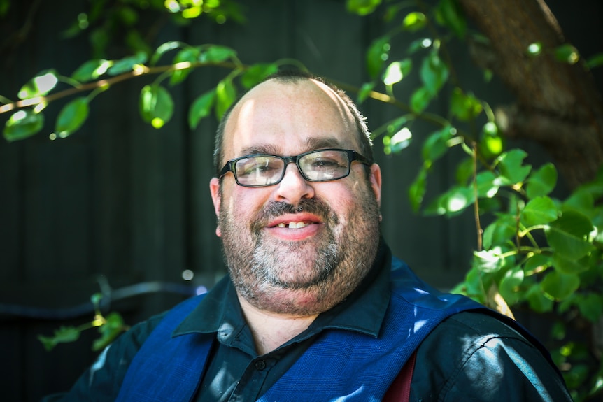 Cameron Bloomfield stands outside in dappled light, smiling at the camera.
