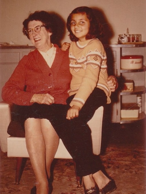An old photo of a young girl sitting on the lap of a woman in a chair, smiling for the camera