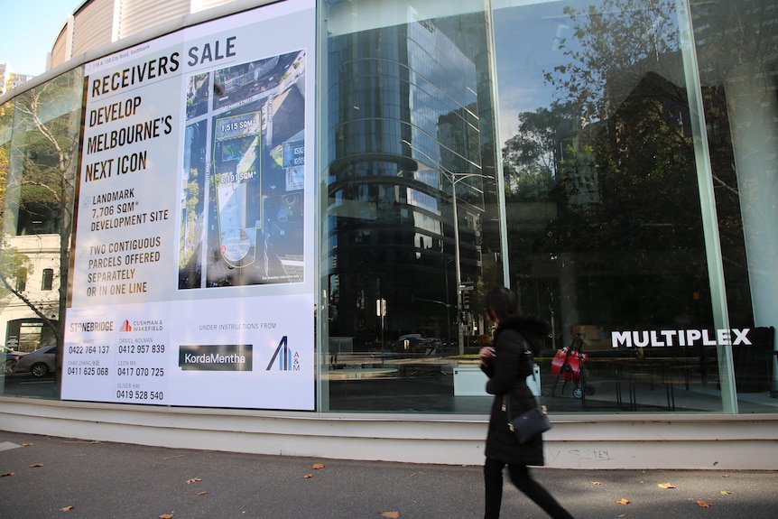 a woman in a black coat walking past a sign saying receivers sale on a building.
