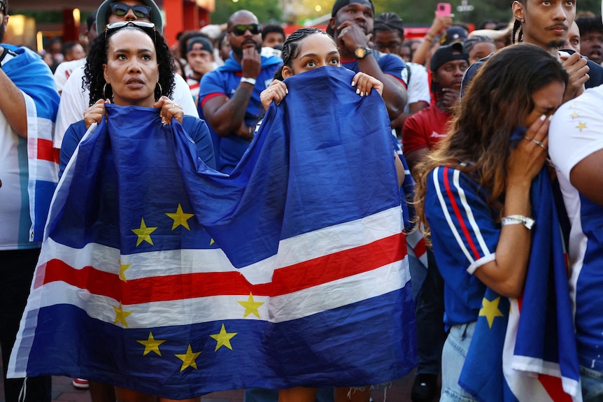 two woman use a carpe verde flag to partially cover their faces, stressed