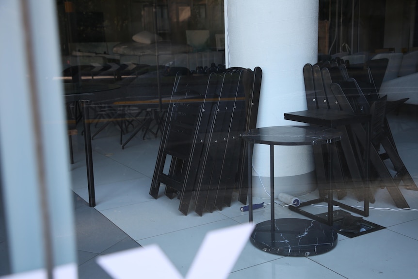 stacks of chairs lean against a pillar behind a glass window.