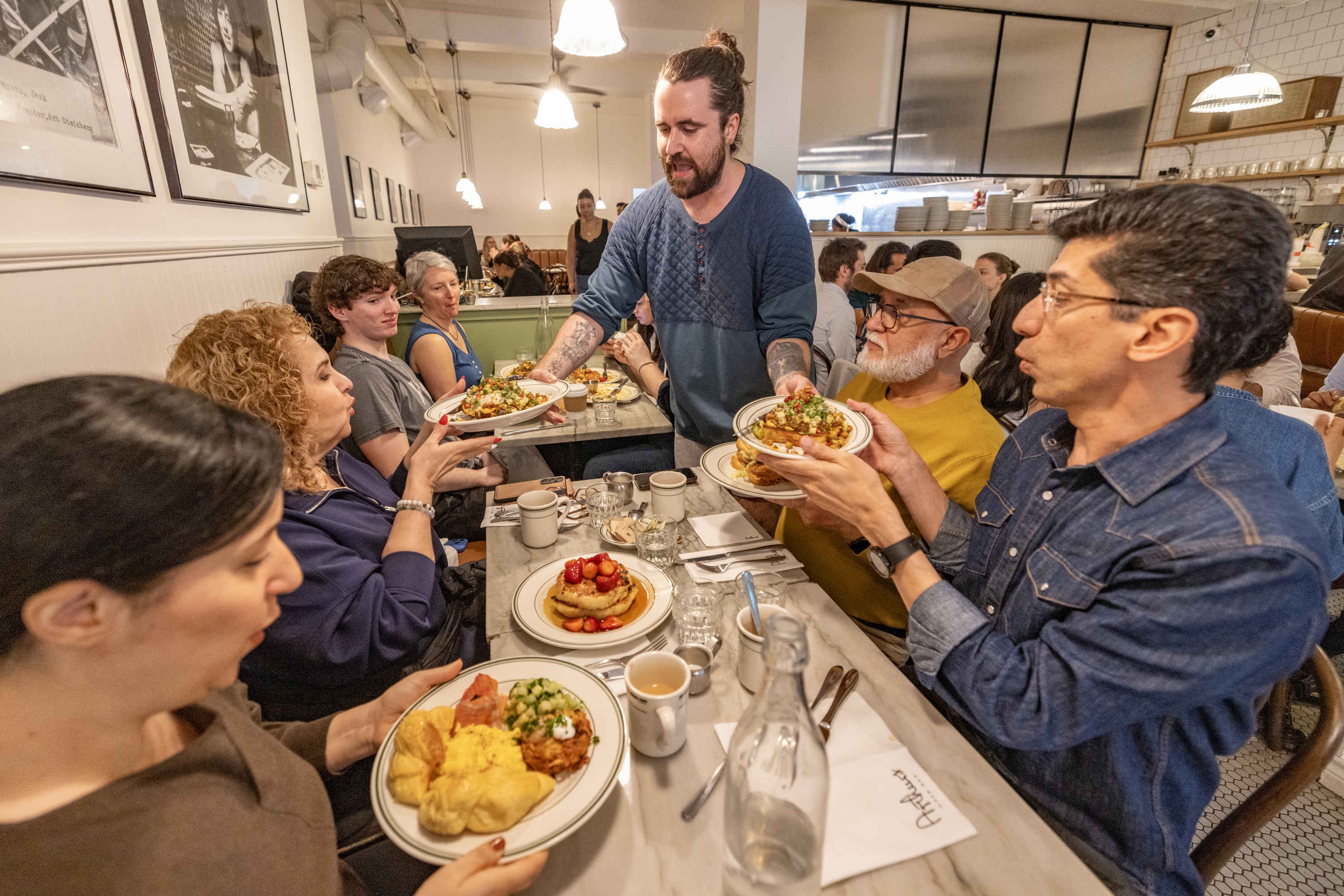 A waiter serves plates of food to a table of four diners in a busy restaurant.