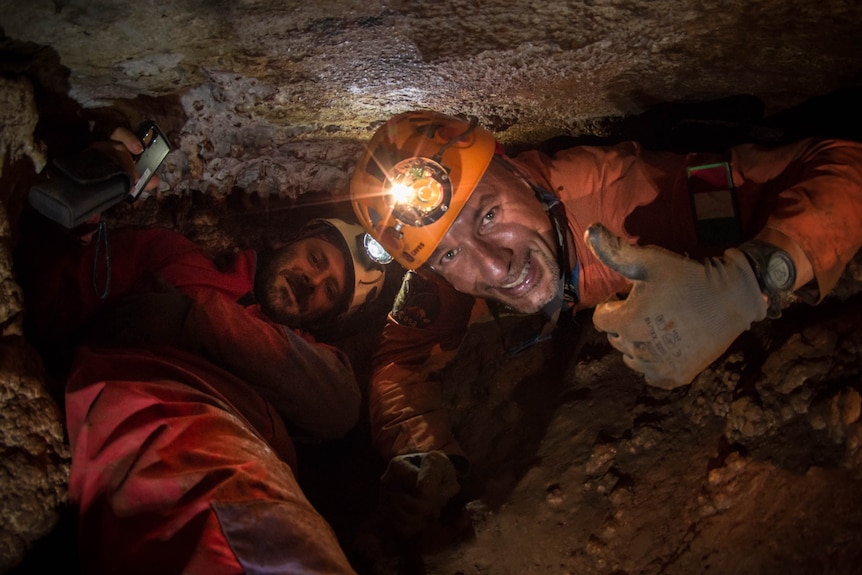 two men with helmets on in a cave.