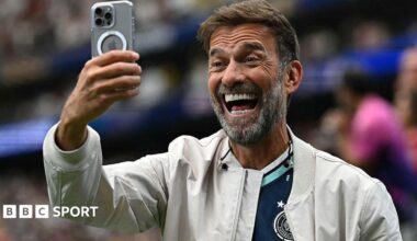 Jurgen Klopp smiling while holding a mobile phone in front of his face