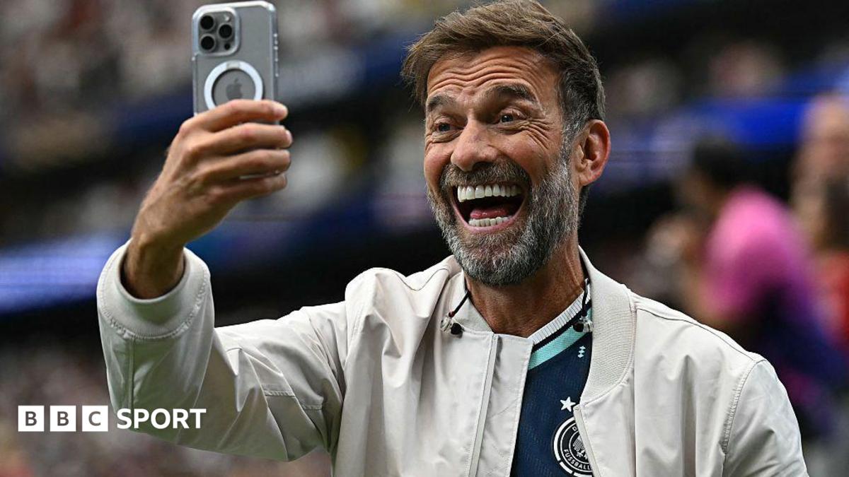 Jurgen Klopp smiling while holding a mobile phone in front of his face