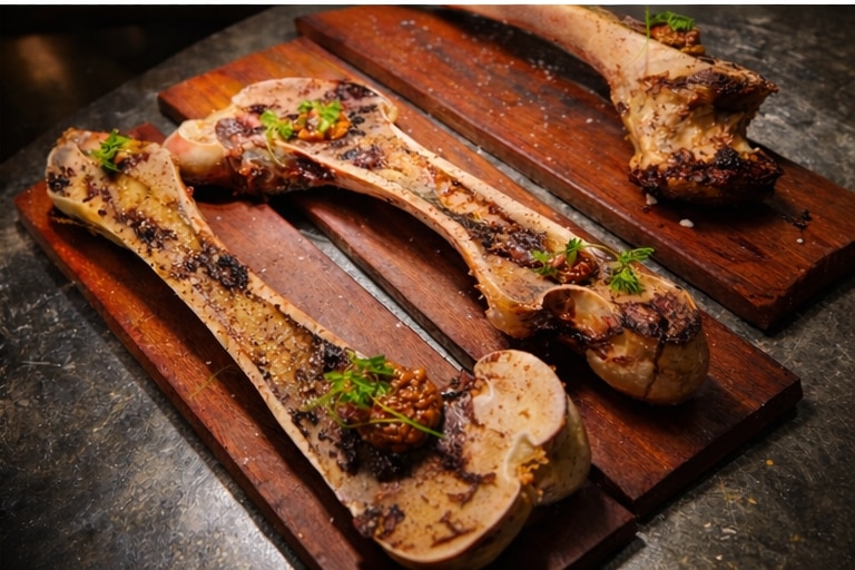 A femur bone sliced in half served on a wood platter with spiced marrow and garlic puree.
