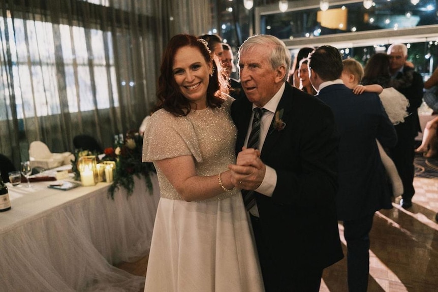 Erin and her dad Steve Mortimer at her wedding, holding each other's hand out front and smiling.