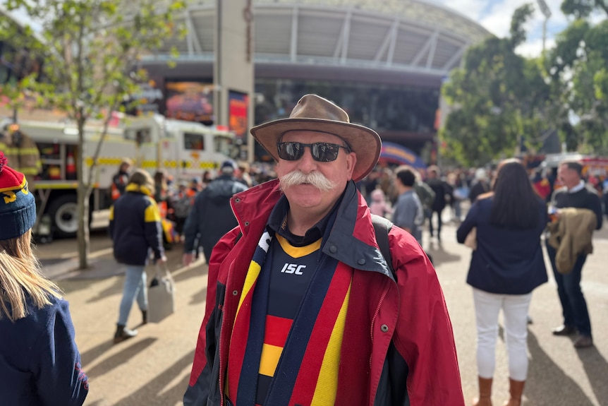 A man with a moustache wearing Crows gear in the forecourt of Adelaide Oval