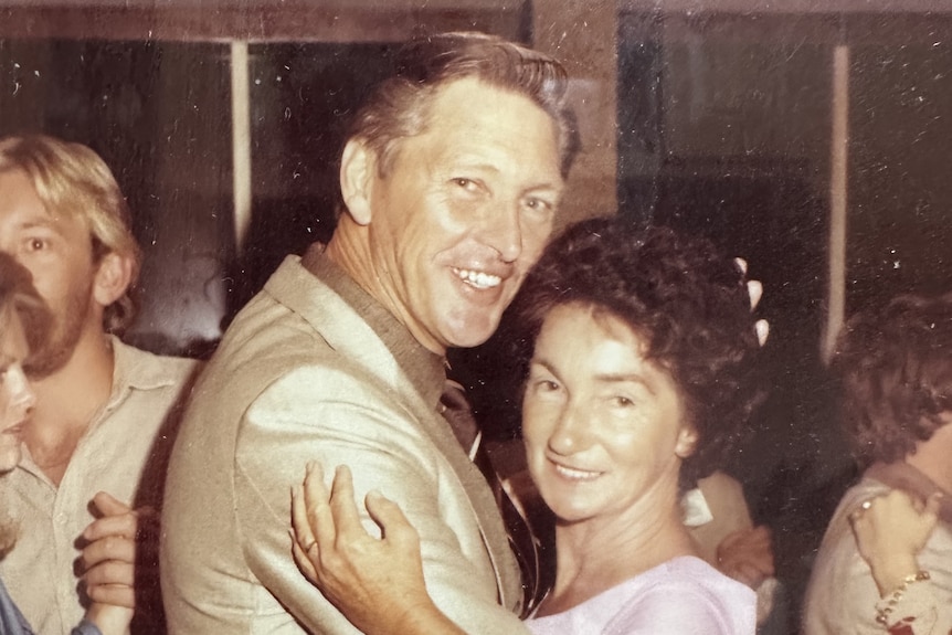 A man and woman in ballroom dancing stance smile at the camera