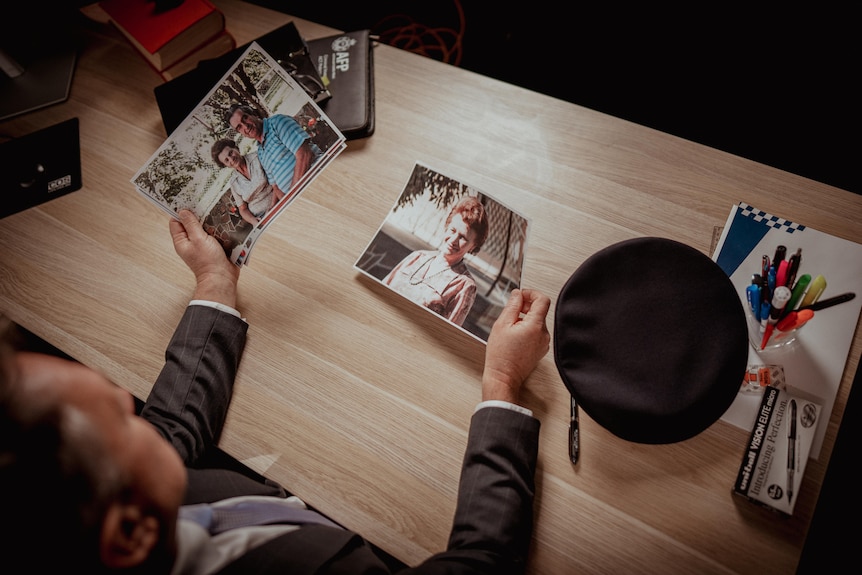 A man in a suit sitting at a desk looking at printouts of photos in his hands.