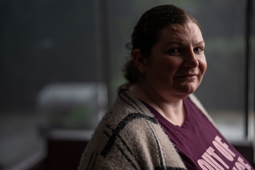 A woman wearing a maroon shirt and checked cardigan looks to her right.