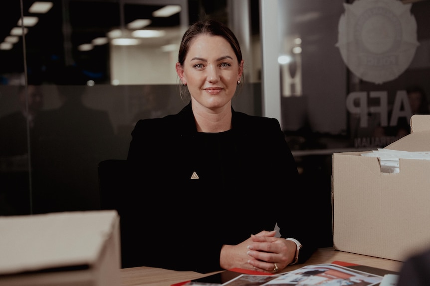 A woman wearing black sitting at a table with boxes of files near her.