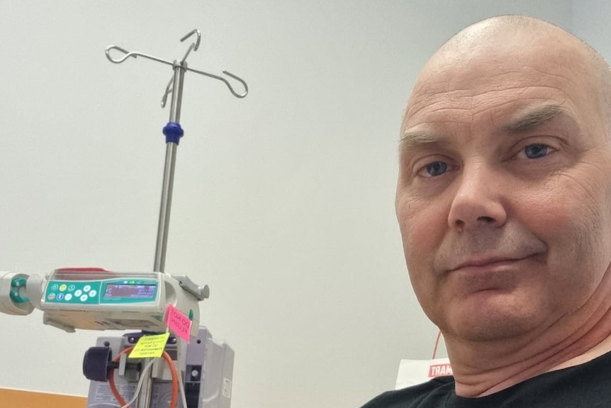 A bald man sitting in a hospital bed.