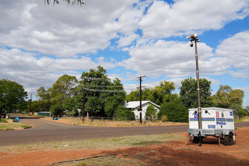 A police storage box unit on the side of the road with security cameras above it, houses in the background.