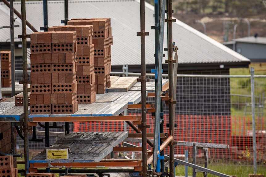 Brown bricks sitting on a scaffold. Temporary fencing can be seen in the background.