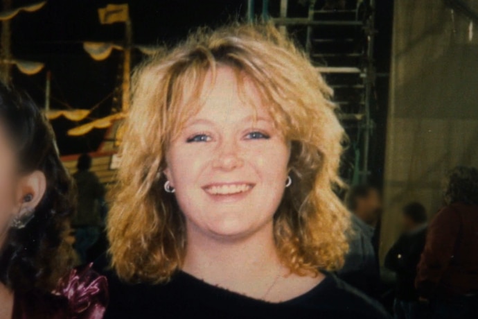 Vintage style picture of a young woman with blonde, feathery hair in an 80s style smiling at the camera