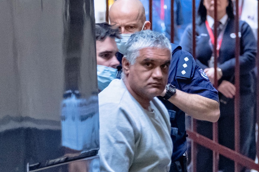 Mohinder Singh is led away from a large black police truck with his hands cuffed.