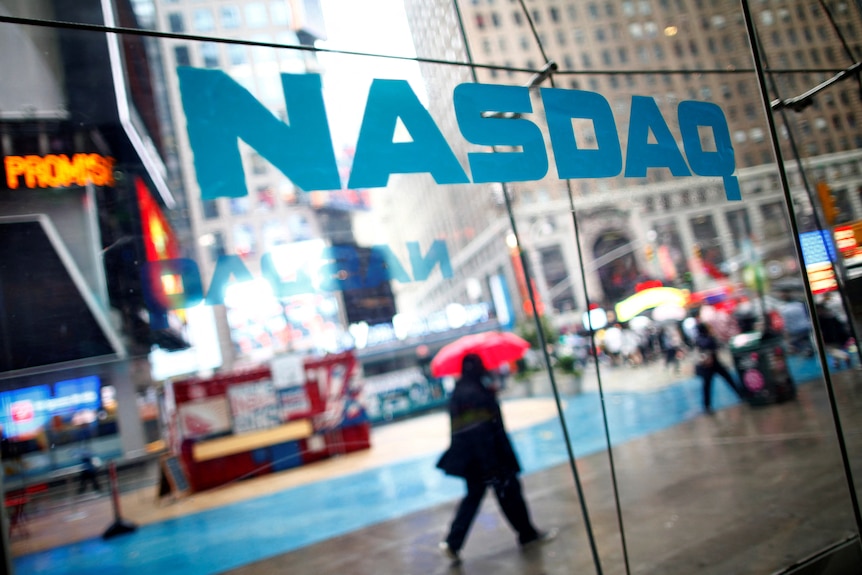 Reflection of person holding umbrella below Nasdaq sign
