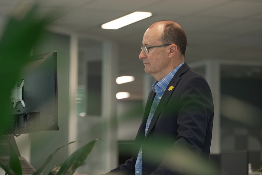 Craig Sinclair working looking at his computer, part of plant blurred to the left