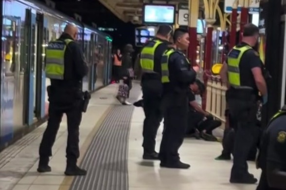 A number of police officers in navy uniforms with bright yellow vests stand on a platform beside a train at night.
