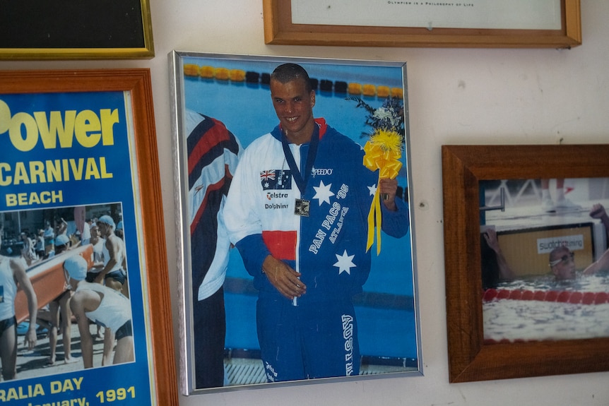 A framed photo of a man wearing an Australian flag tracksuit with a gold medal around his neck in front of a swimming pool.