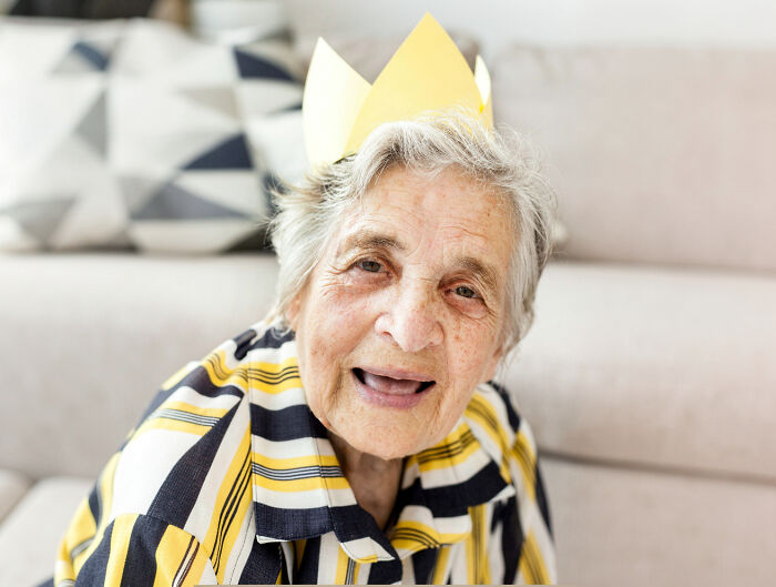 An elderly woman smiling and wearing a paper crown, reflecting the unexplained things nurses witness with patients.
