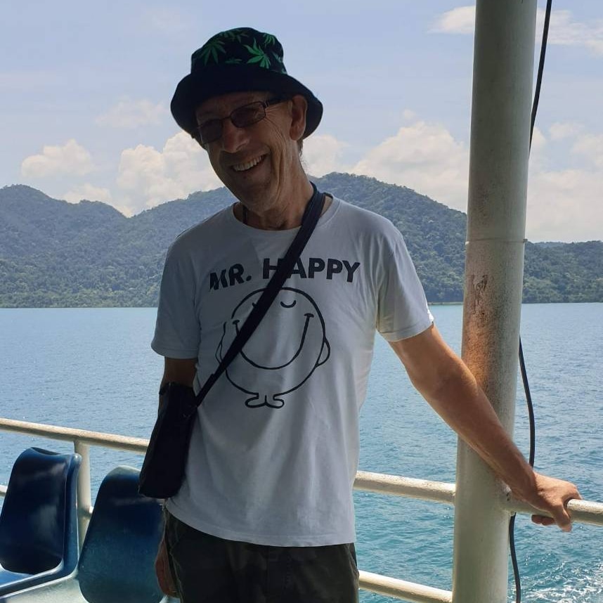 A happy-looking male of pension age in a bucket hat and white tee on a boat in tropical surrounds.