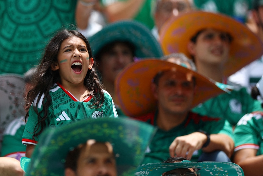in a crowd of mexican fans a young girl sits on someone's shoulders cheering