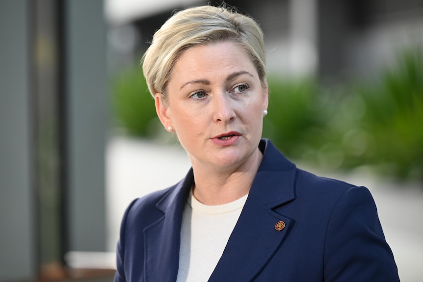 A woman with short blonde hair in blue jacket speaking to right of frame.